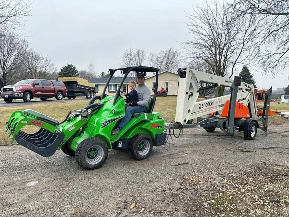 A man is driving a green tractor with a bucket attached to it.