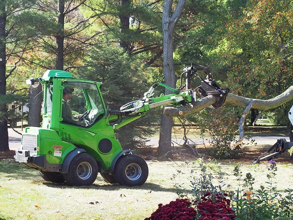 A green tractor is cutting a tree branch in a park