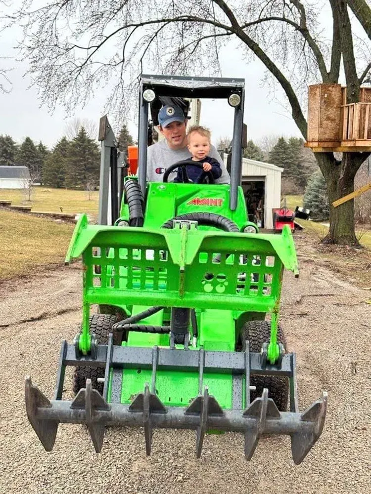 A man and a baby are riding a green tractor.