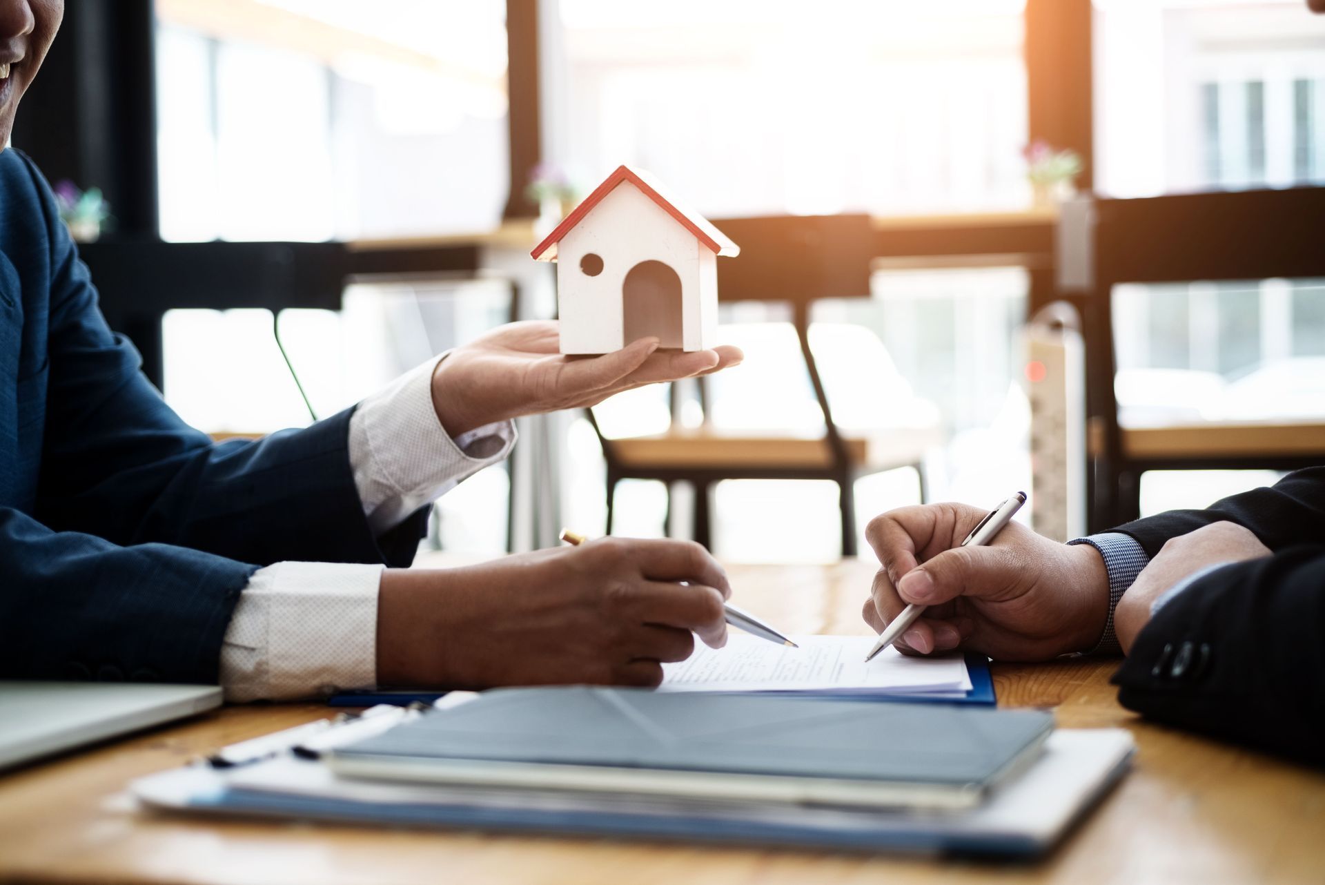 A woman is holding a small house in her hand while a man is signing a document.