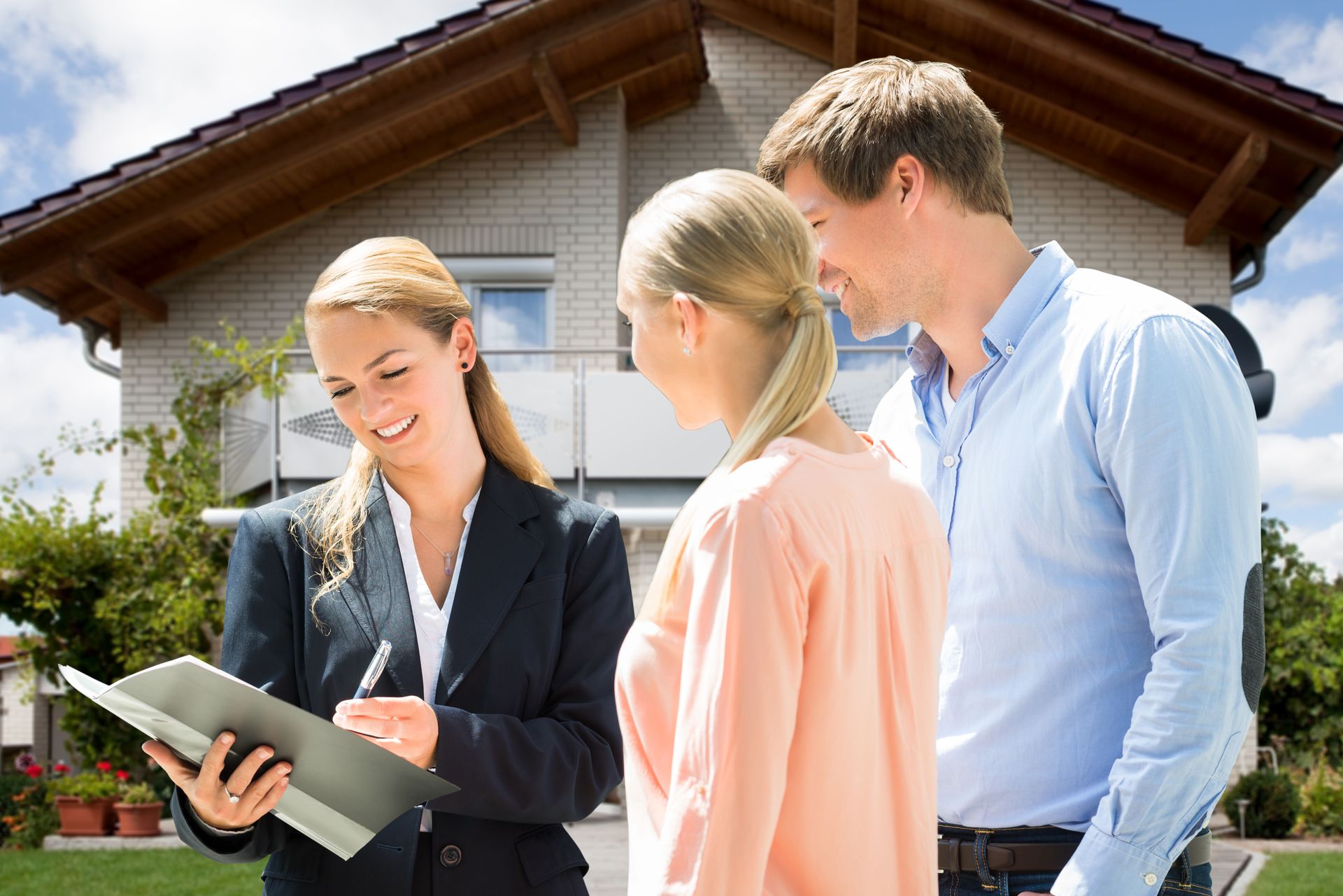 A woman is holding a clipboard and talking to a man and woman in front of a house.
