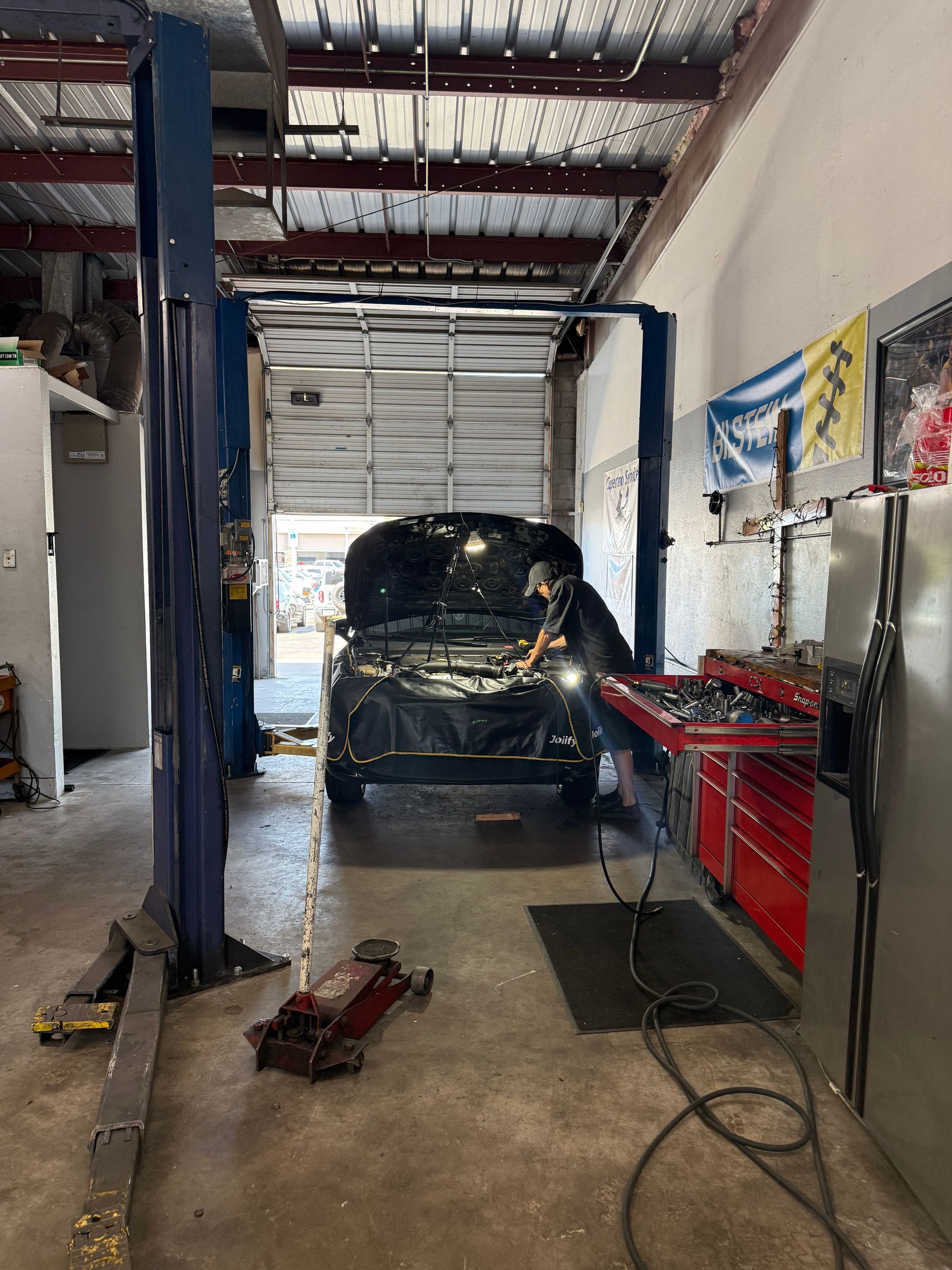 Auto repair shop with a car on a lift, tools on the floor, and a red tool chest along the wall