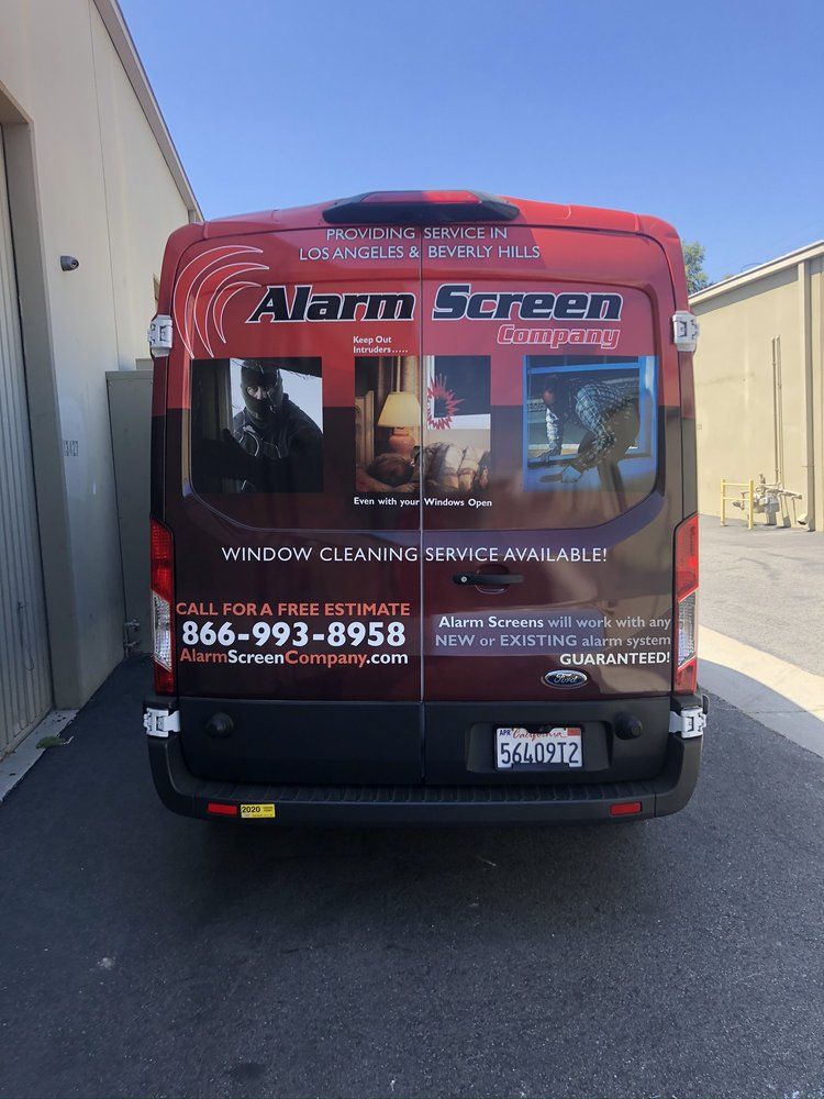 Red service van for Alarm Screen parked in an alley, with large promotional graphics on the back.