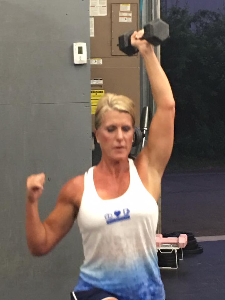 A woman is lifting a dumbbell over her head in a gym.