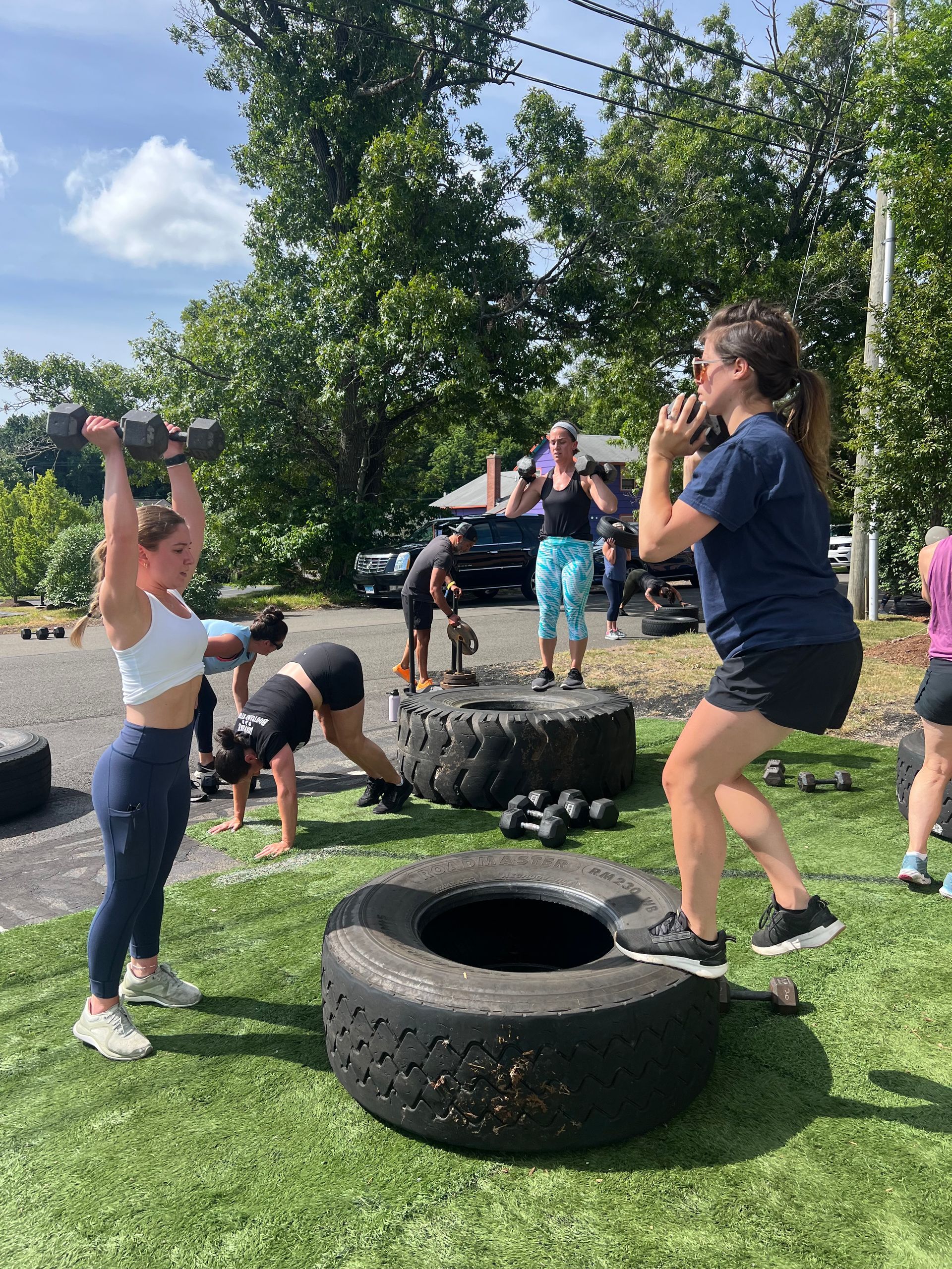 A group of people are doing exercises with dumbbells and tires.