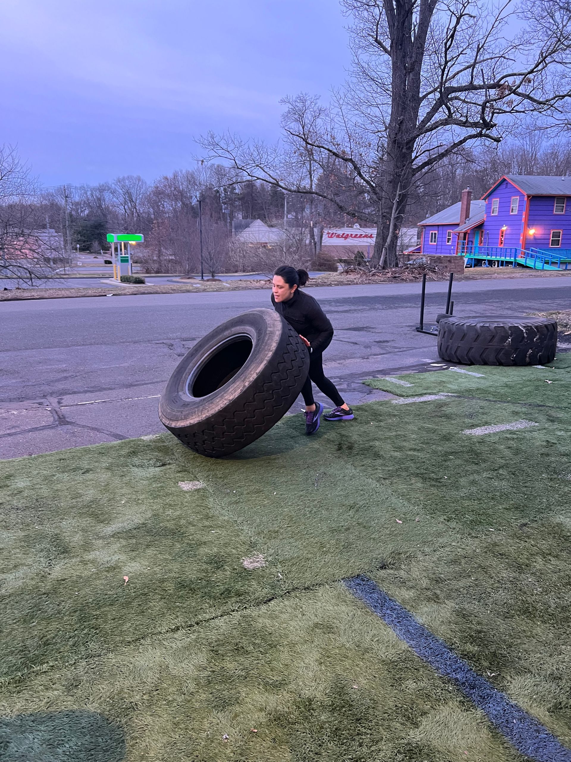 A woman is pushing a tire on a grassy field.