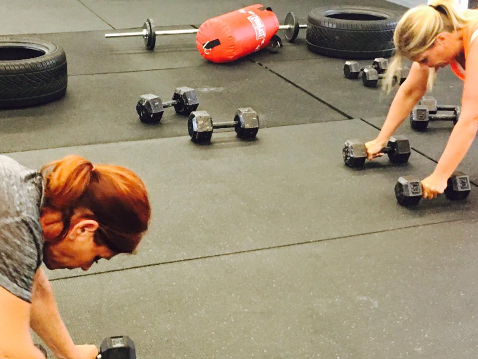 Two women are doing push ups with dumbbells in a gym