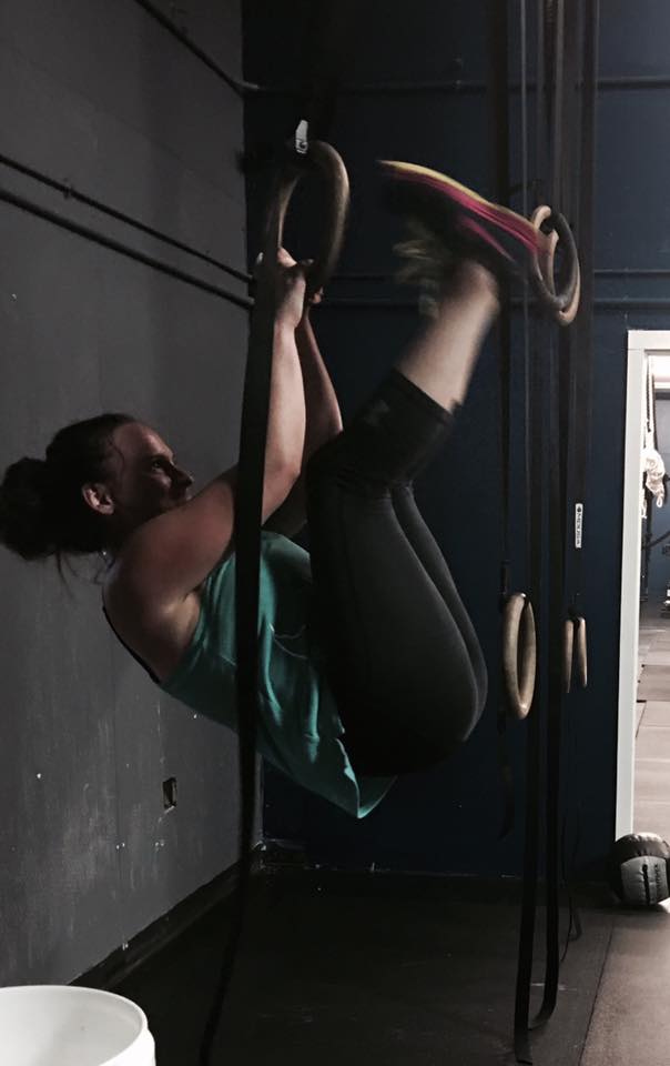 A woman is doing a pull up on a bar in a gym.