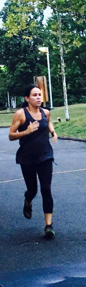 A woman in a black tank top is running down a street