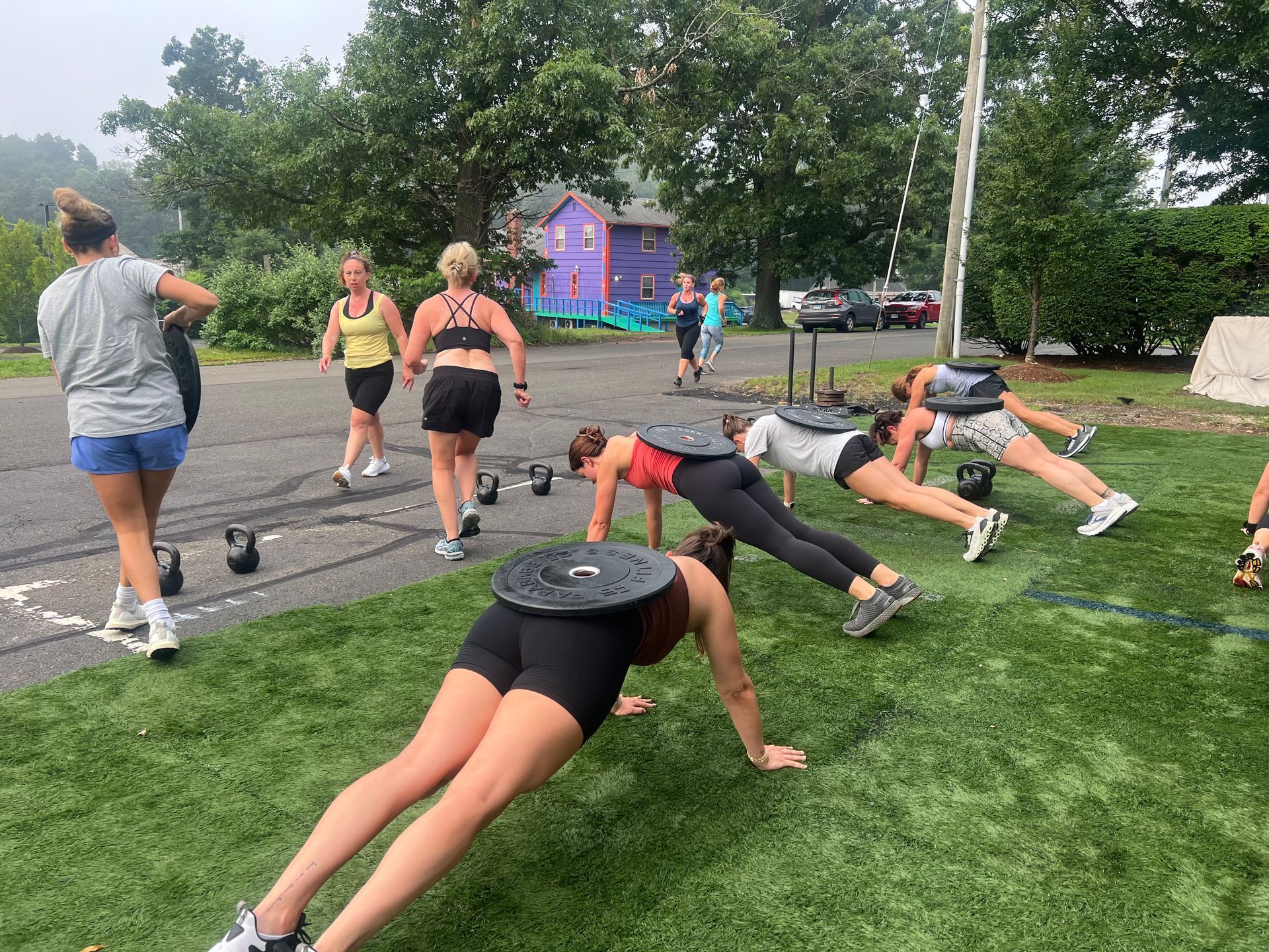 People doing plank exercises outdoors on grass near a track and trees