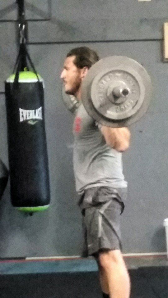 A man is squatting with a barbell in front of an everlast bag