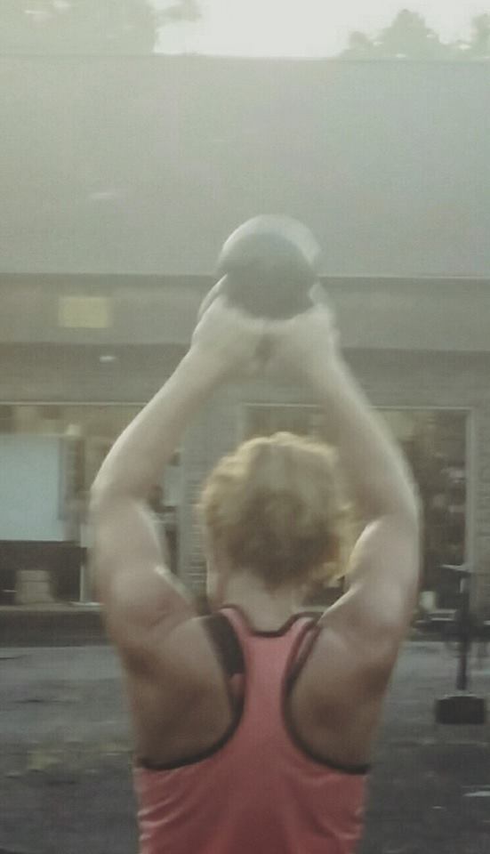 A woman is lifting a kettlebell over her head.