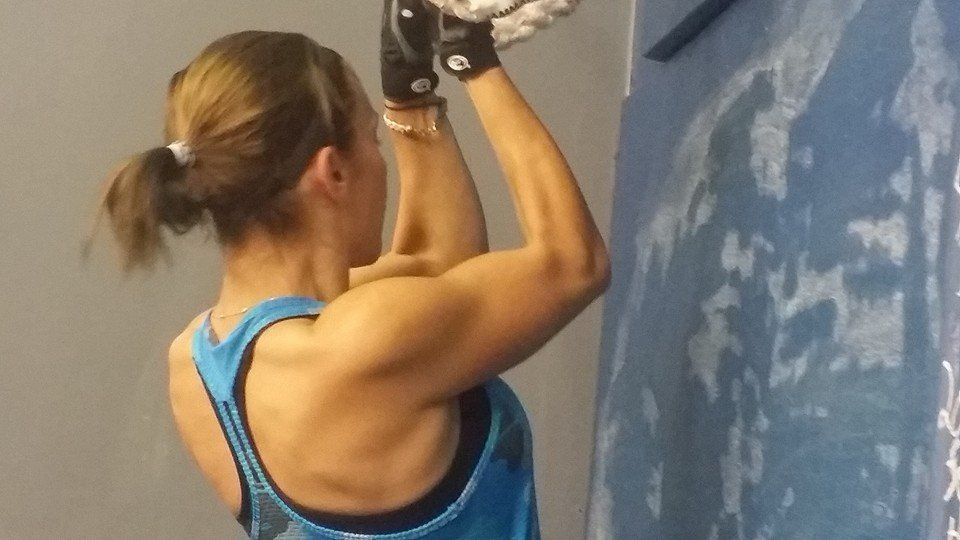 A woman in a blue tank top is doing a pull up on a bar.