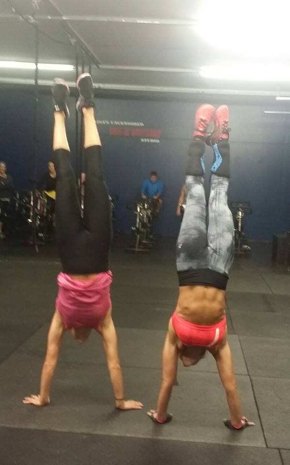 Two women are doing handstands in a gym