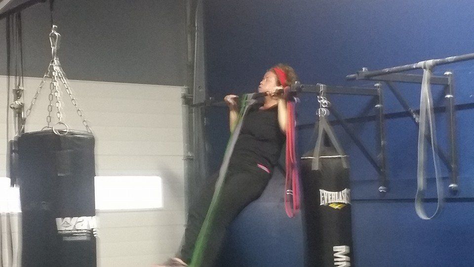 A woman is doing pull ups with a resistance band in a gym.