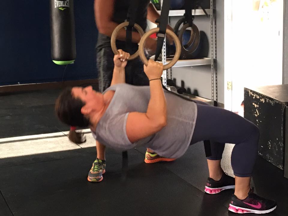 A woman is doing push ups on gymnastic rings in a gym.