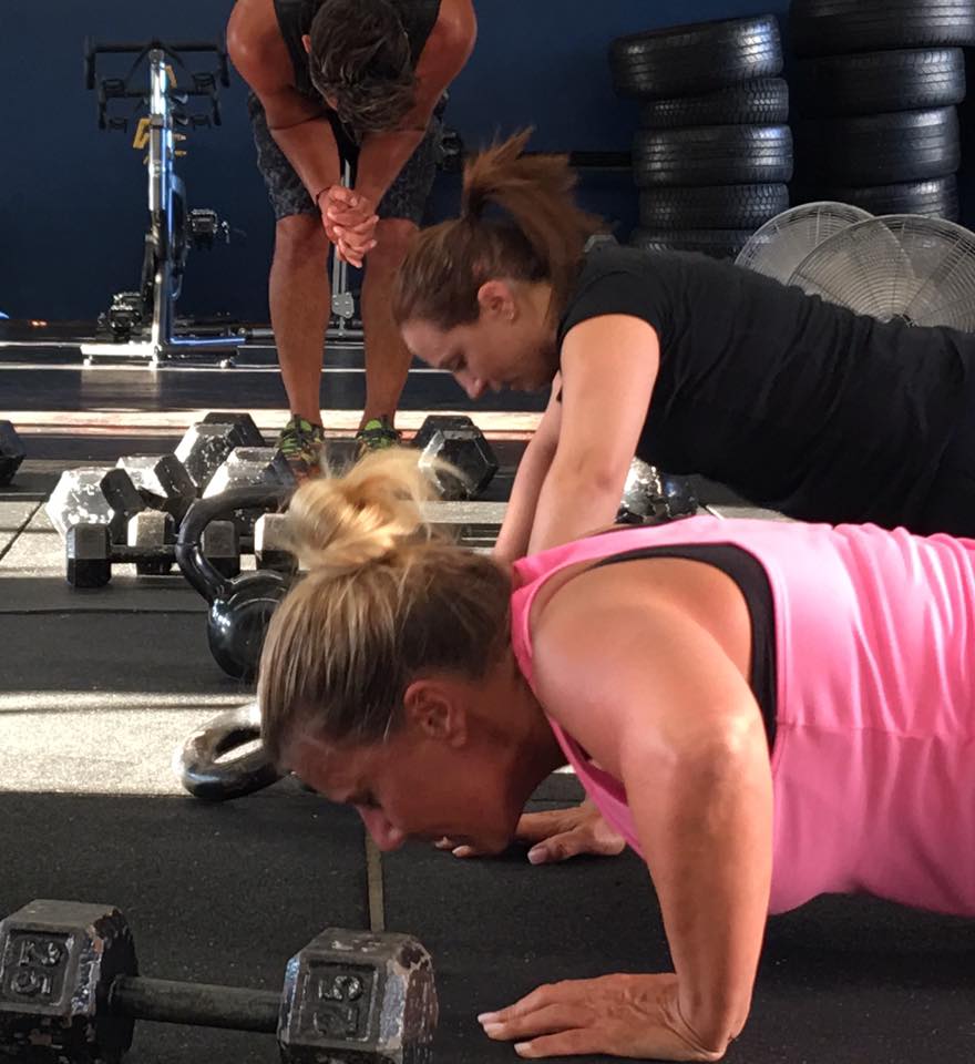 Two women are doing push ups in a gym