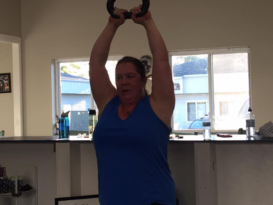 A woman is lifting a kettlebell over her head in a gym.