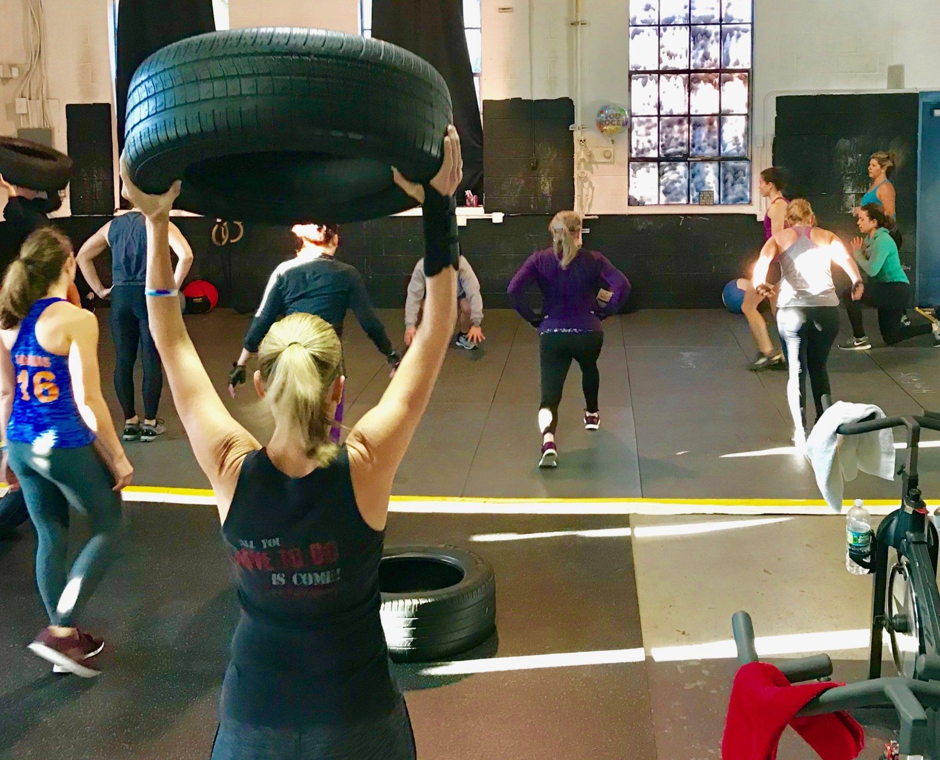 A woman is lifting a tire over her head in a gym.
