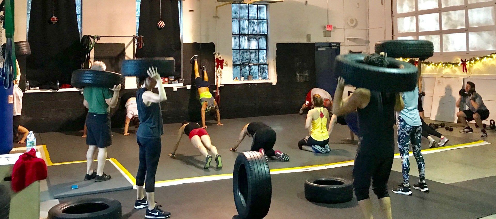 A group of people are doing exercises with tires in a gym.