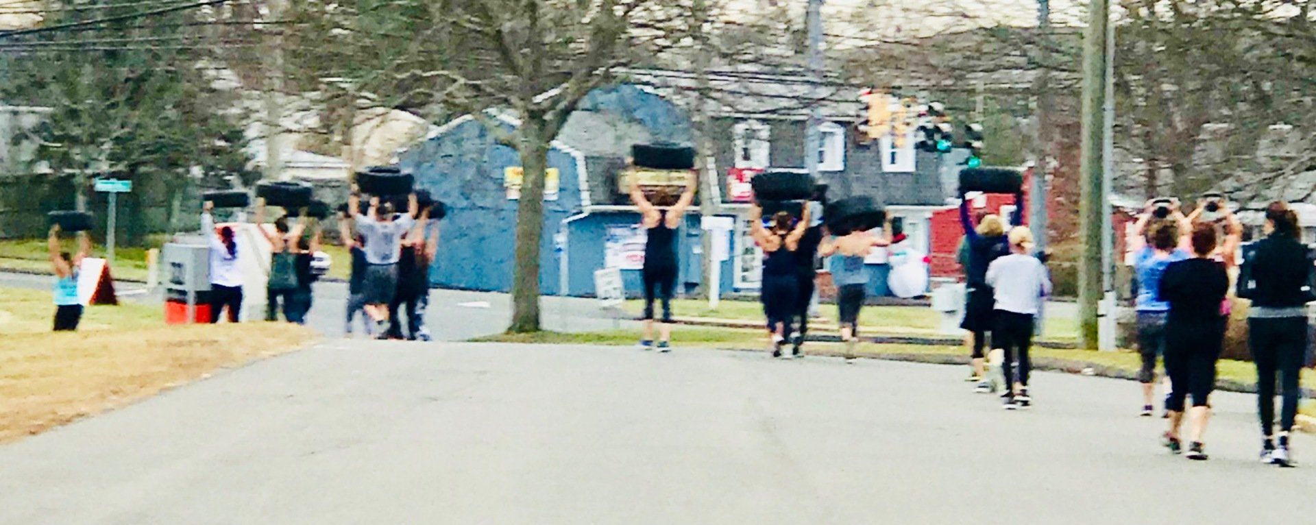 A group of people are walking down a street carrying tires on their shoulders.