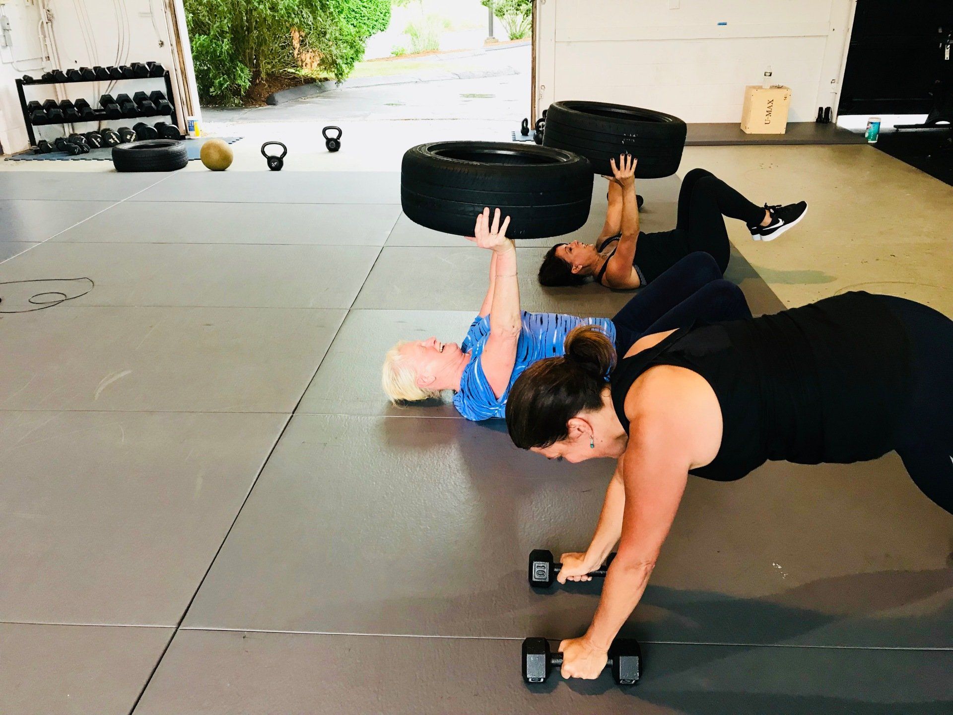 Three women are doing push ups with dumbbells in a gym.
