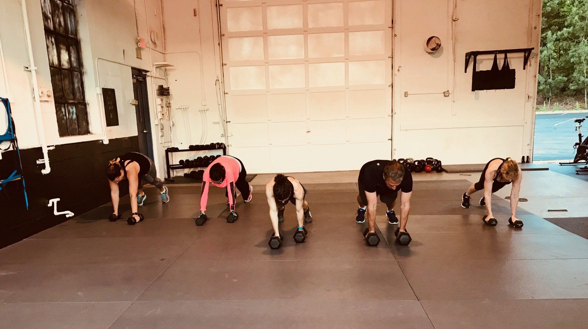 A group of people are doing push ups with dumbbells in a gym.