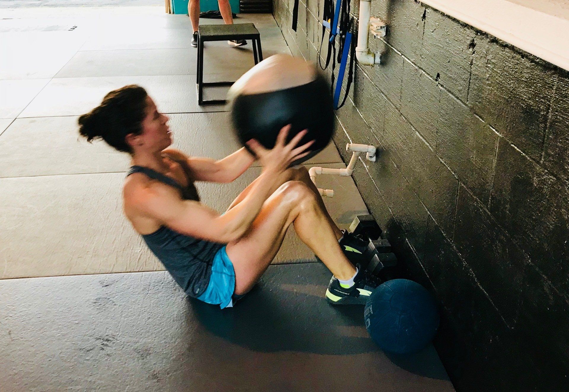 A woman is sitting on the floor holding a medicine ball.