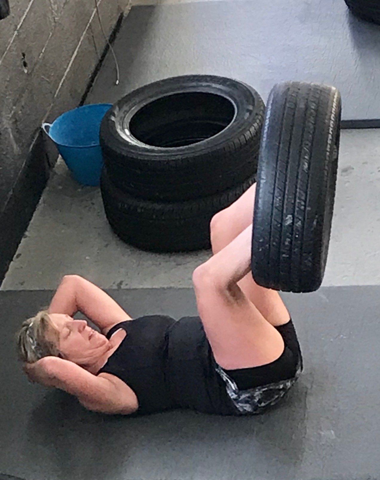 A woman is laying on the floor with a tire on her legs.