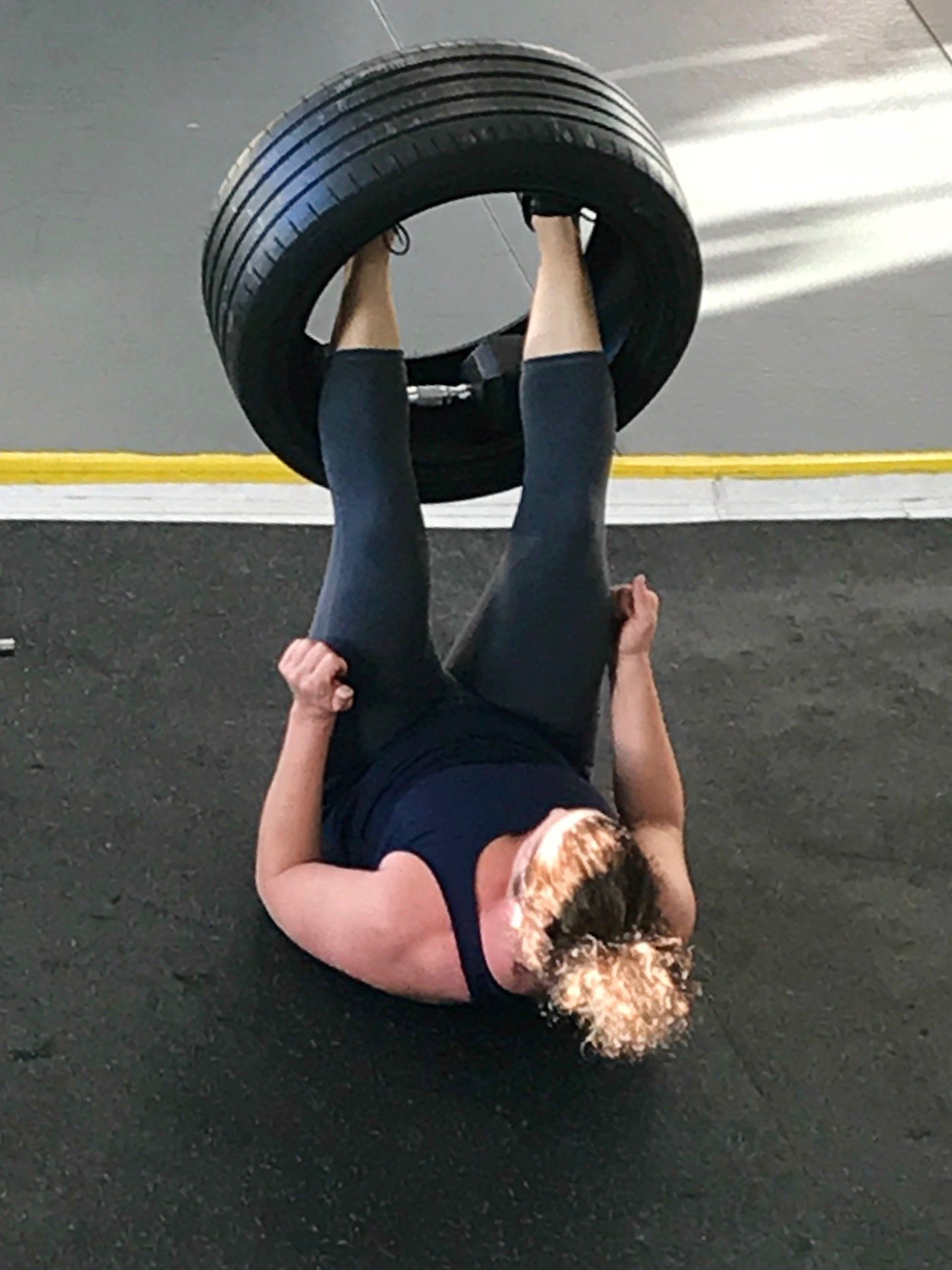 A woman is doing exercises with a tire on her head