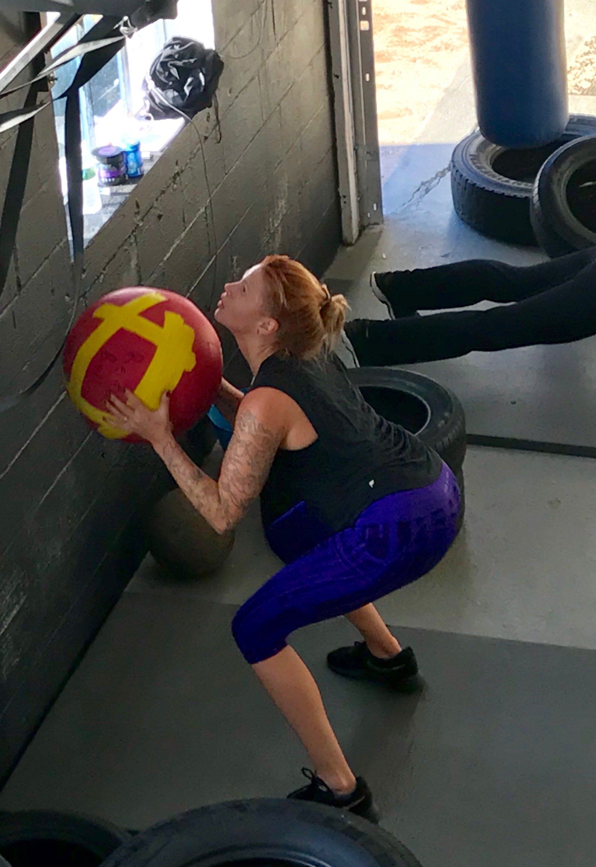 A woman squatting down holding a red and yellow ball