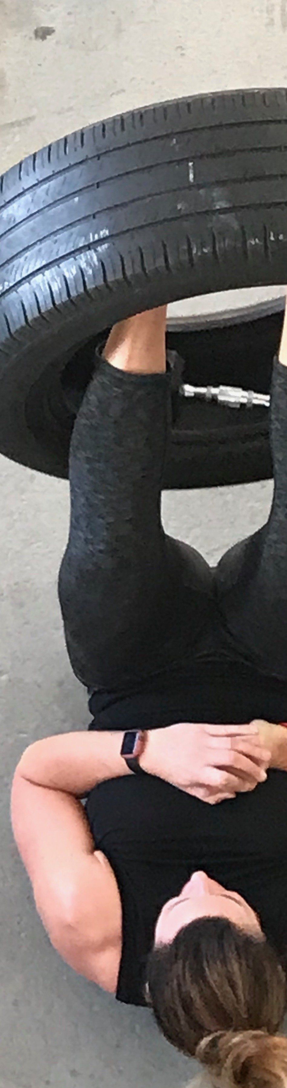 A woman is laying on her stomach with a tire on her head.