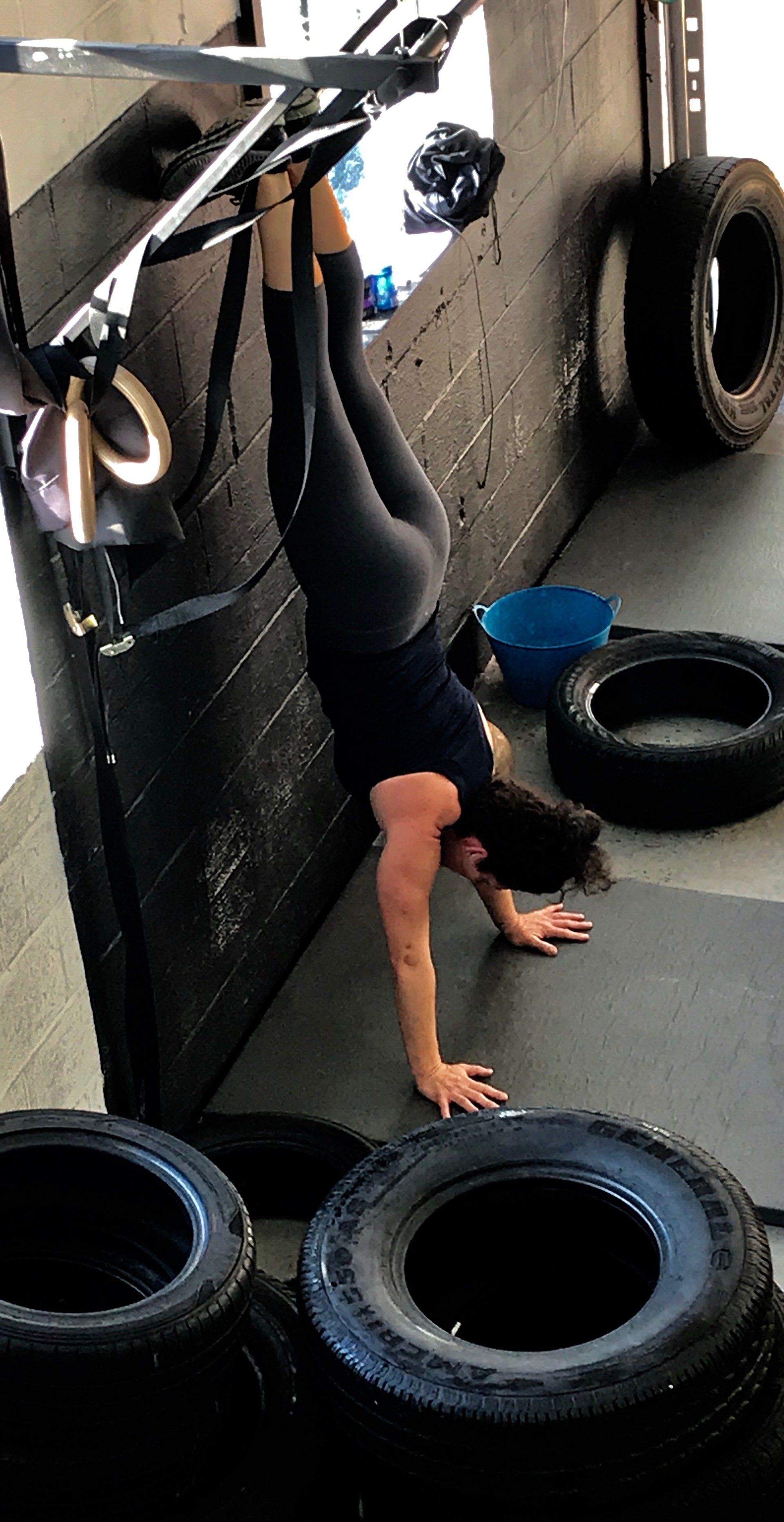 A woman is doing a handstand in a gym surrounded by tires.