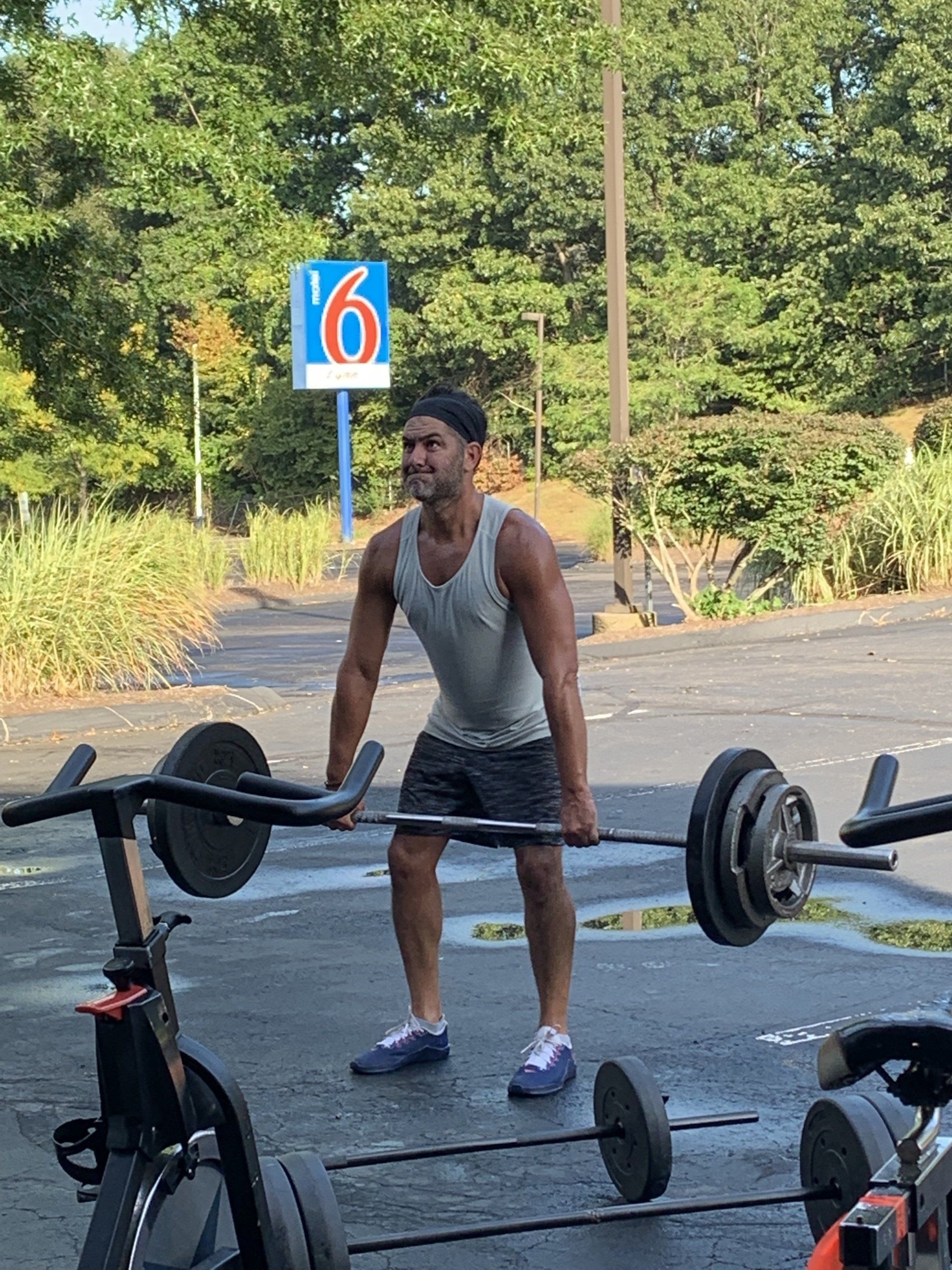 A man is lifting a barbell in a parking lot.