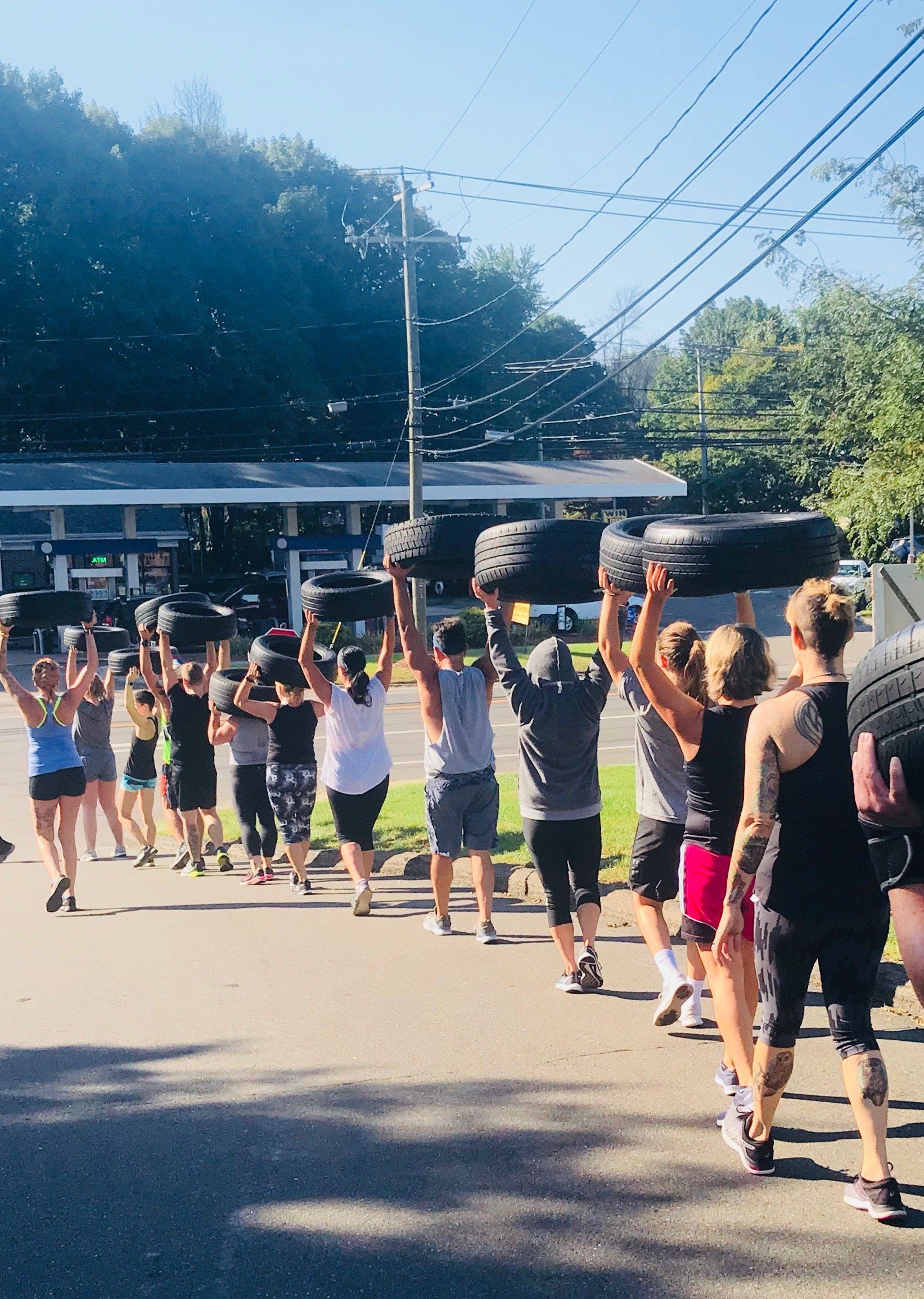 A group of people are walking down a street carrying tires on their shoulders.