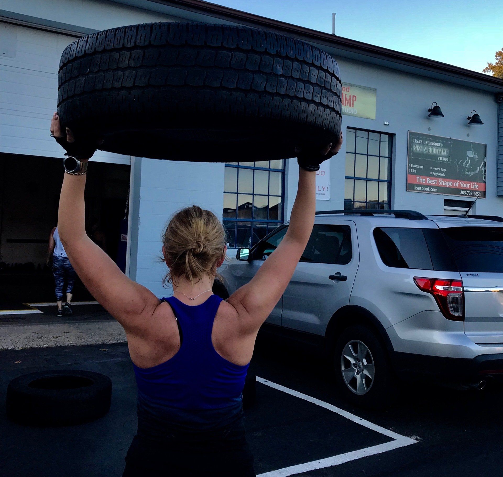 A woman is holding a large tire over her head