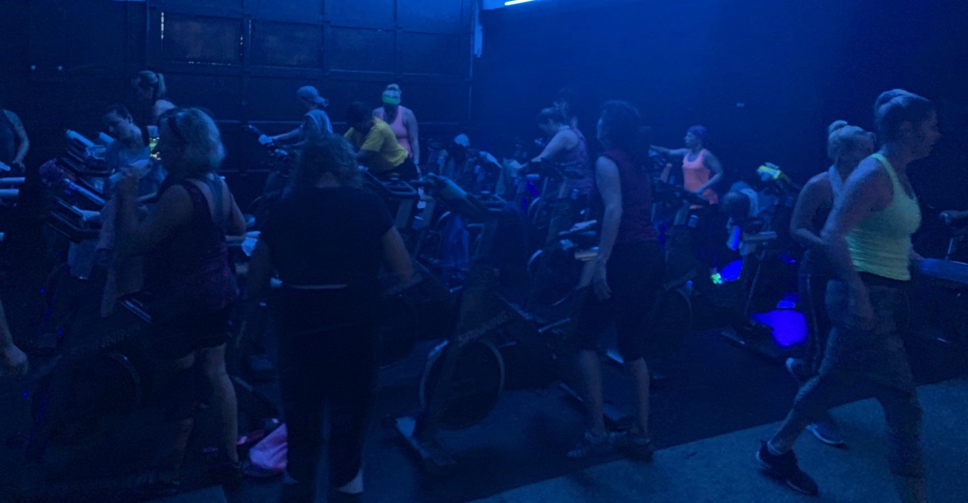 A group of people are riding exercise bikes in a dark room.