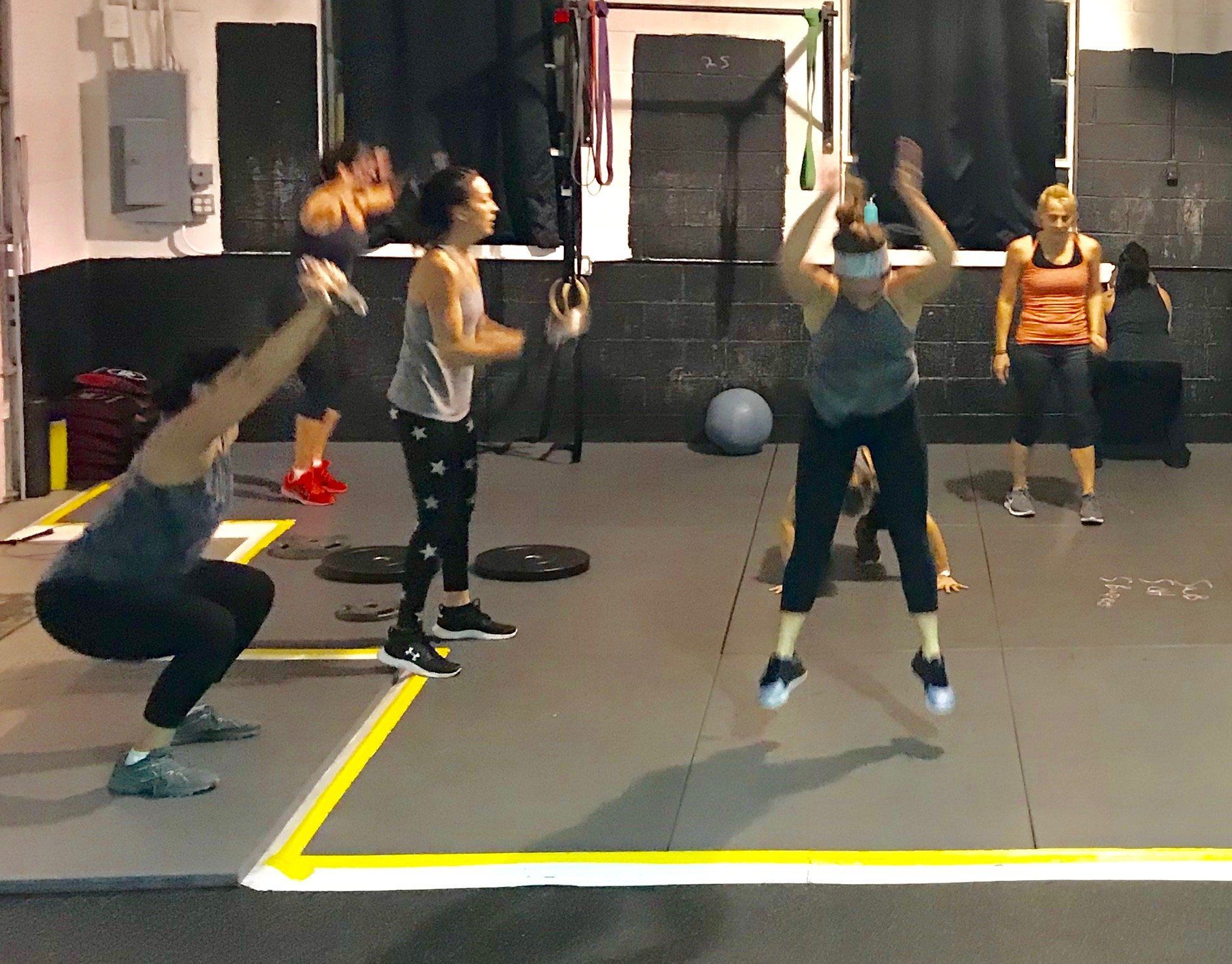 A group of women are doing squats and jumping in a gym.