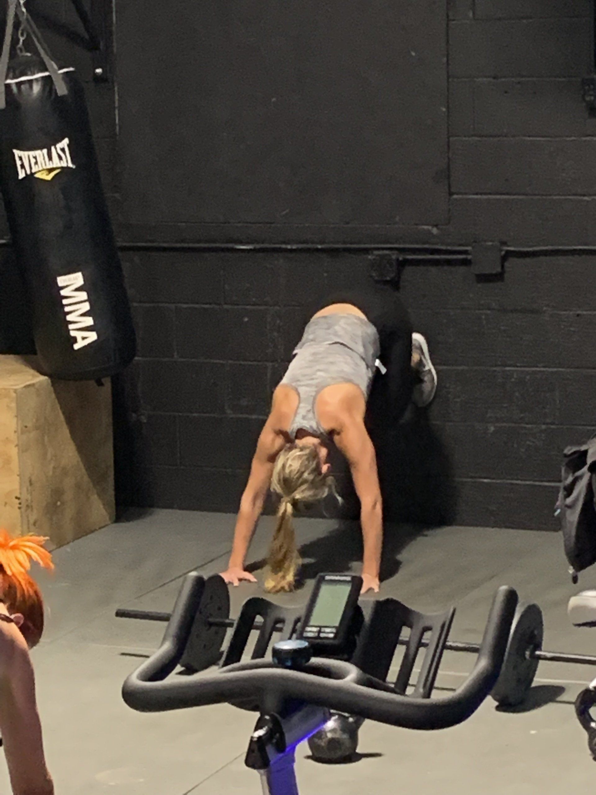 A woman is doing a handstand on an exercise bike in a gym