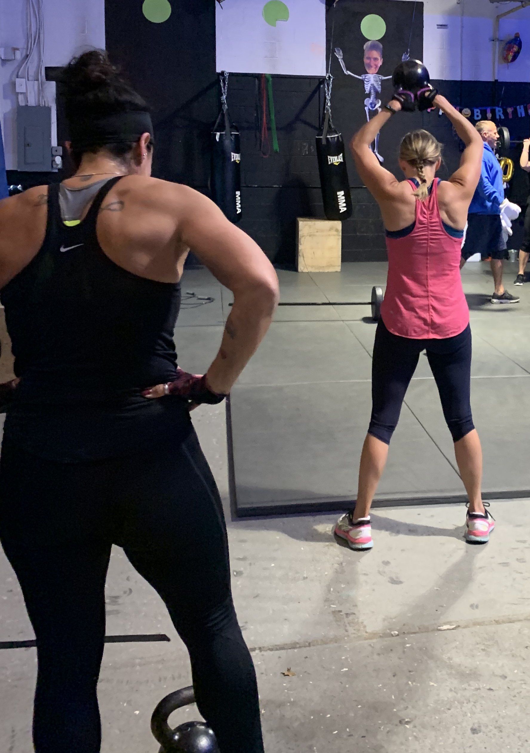 A woman in a pink tank top is holding a kettlebell over her head