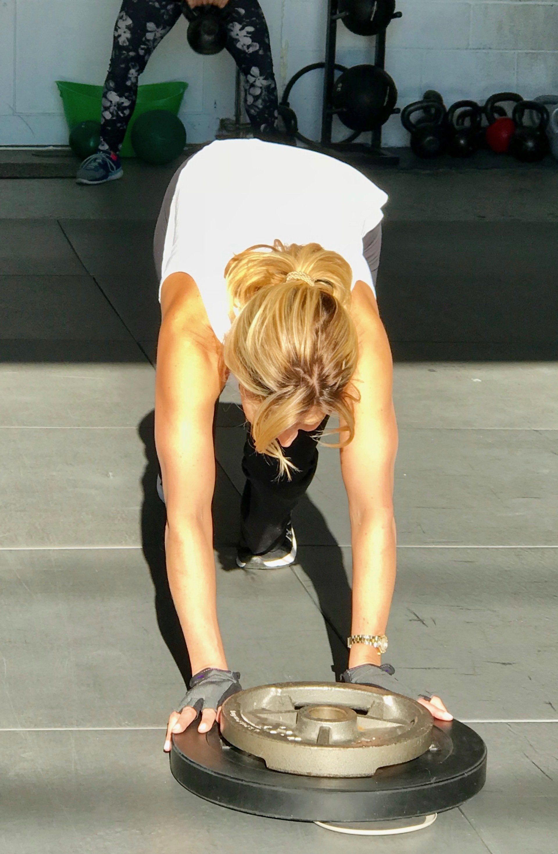 A woman is bending over to push a barbell on a tire.