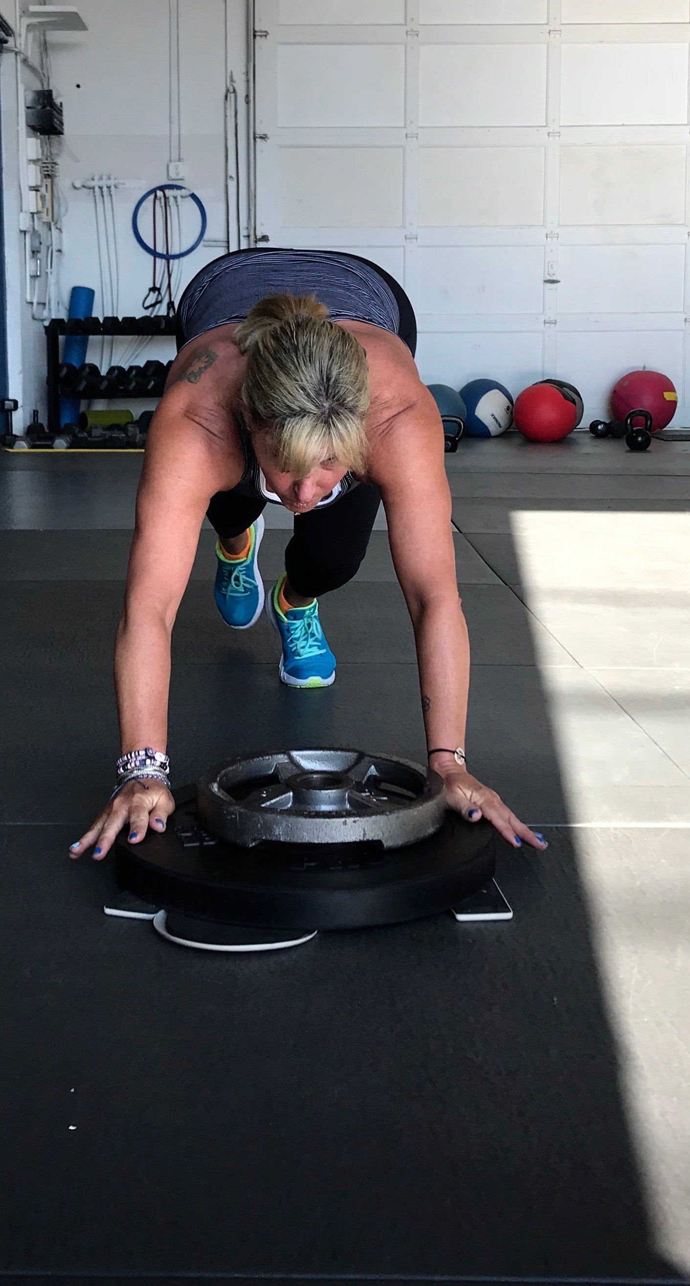 A woman is doing push ups on a weight plate in a gym.