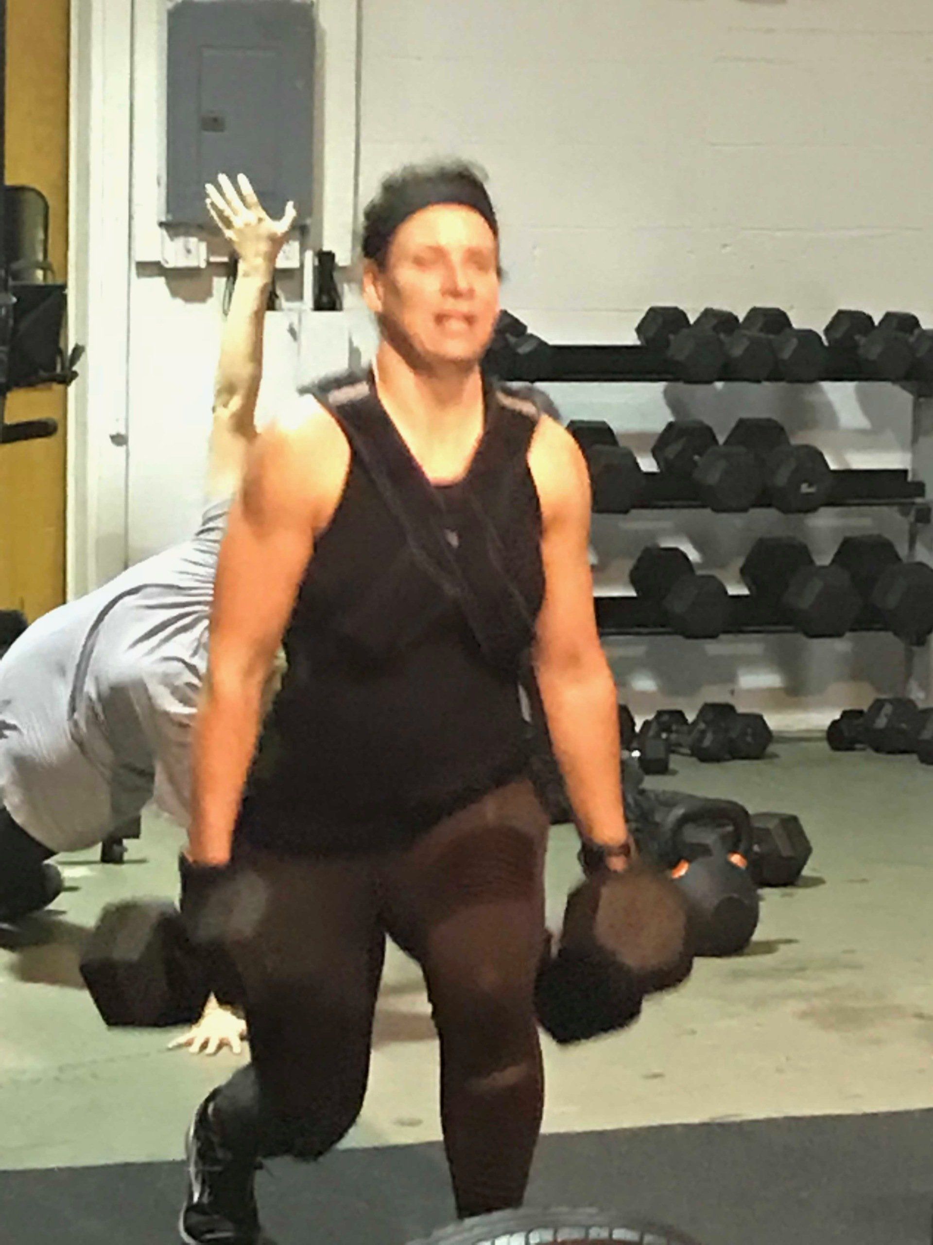 A man in a black tank top is holding a pair of dumbbells in a gym