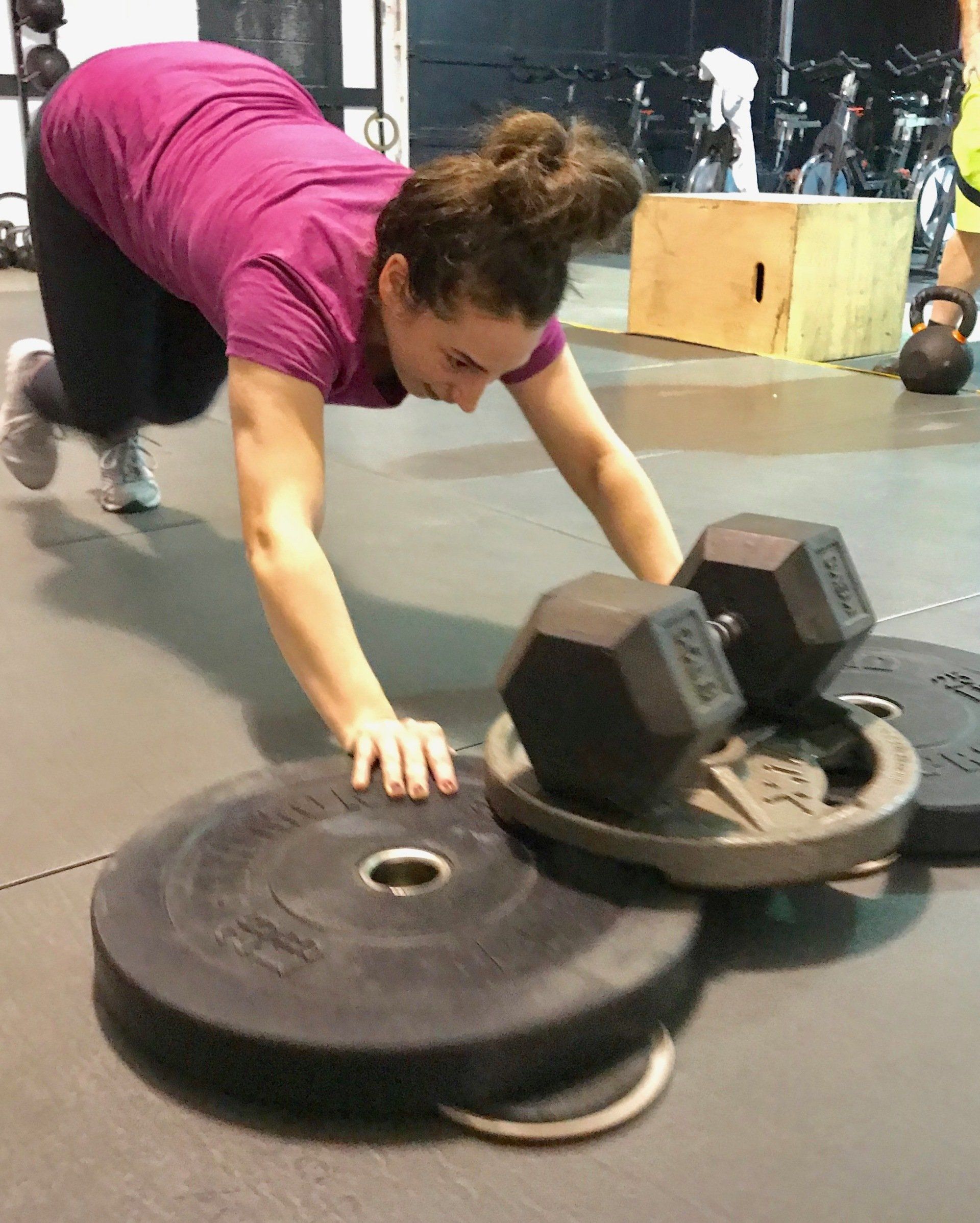 A woman is doing push ups with dumbbells on top of plates in a gym.
