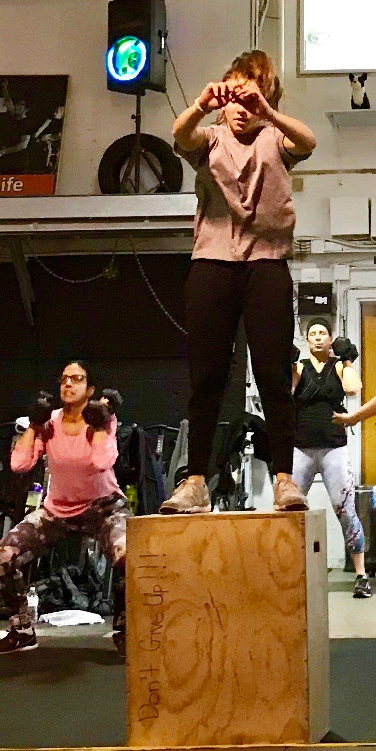 A woman is standing on top of a wooden box in a gym.