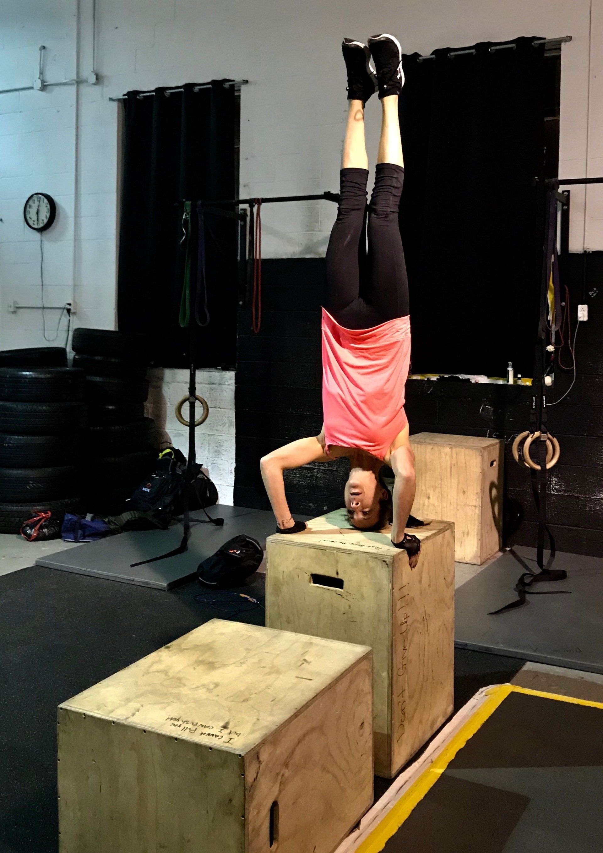 A woman is doing a handstand on a box in a gym.