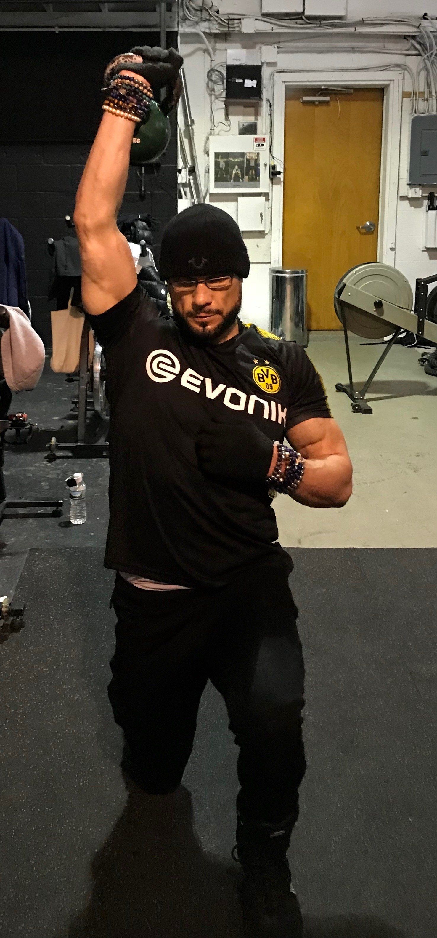 A man wearing a black evon t-shirt is lifting a kettlebell in a gym.