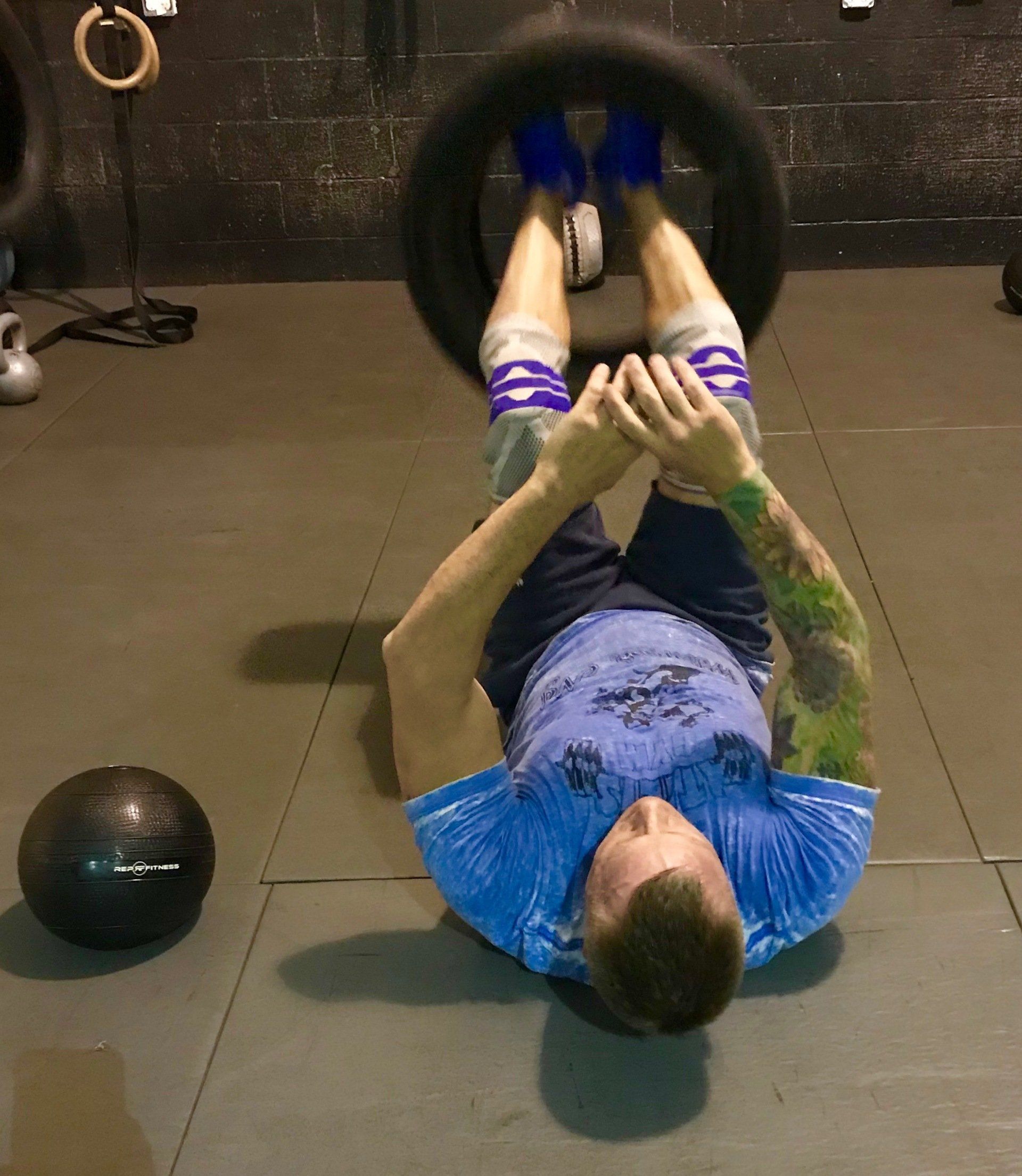 A man in a blue shirt is laying on his back holding a tire