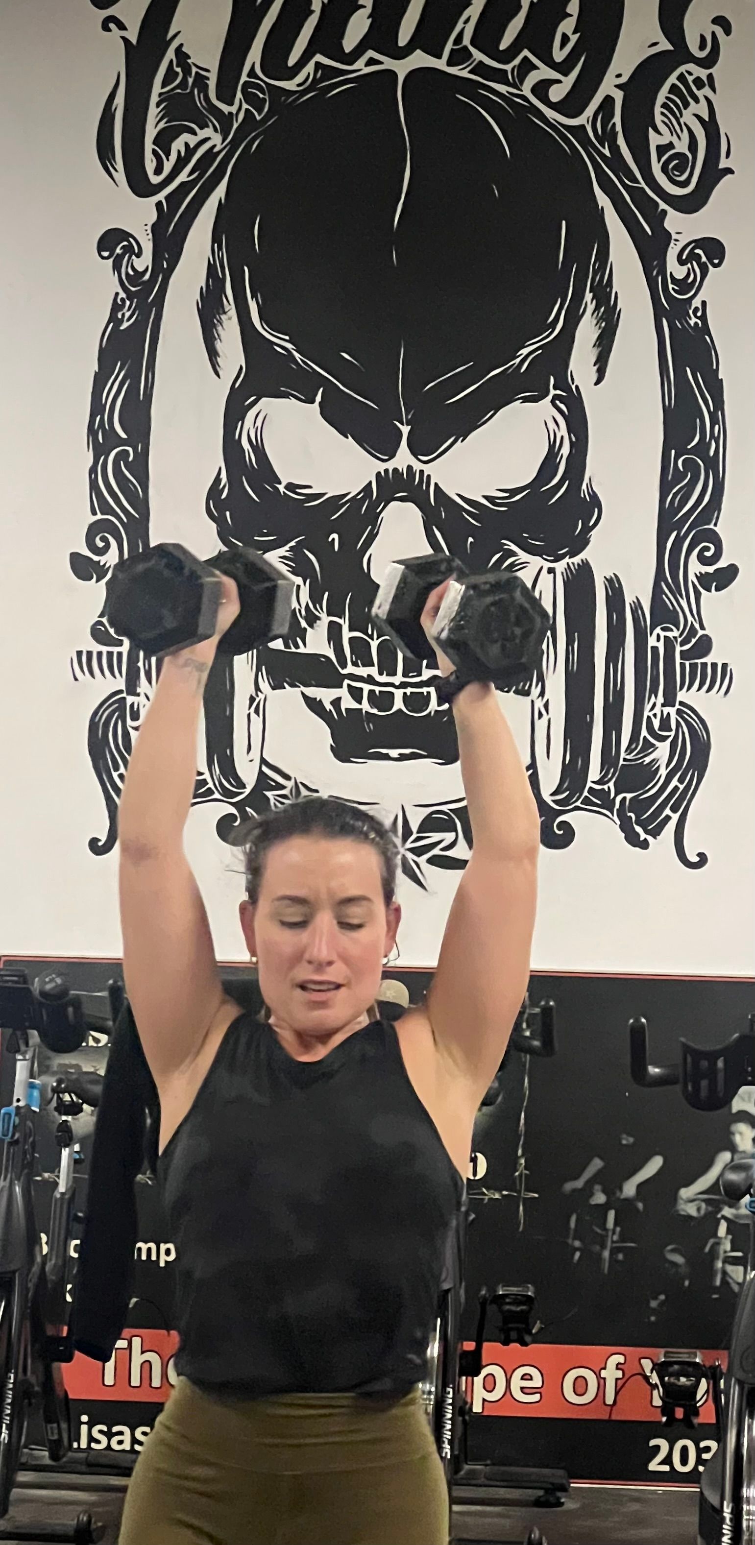 A woman is lifting a dumbbell over her head in a gym.