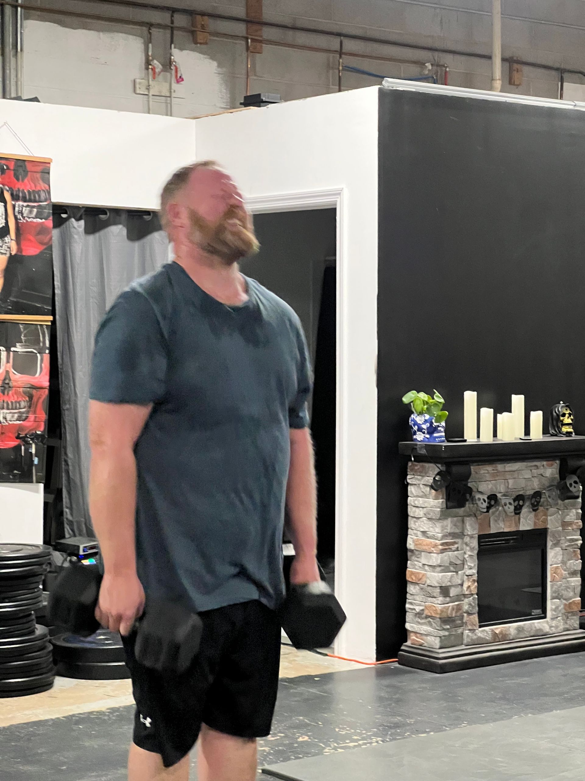 A man with a beard is holding a dumbbell in a gym.